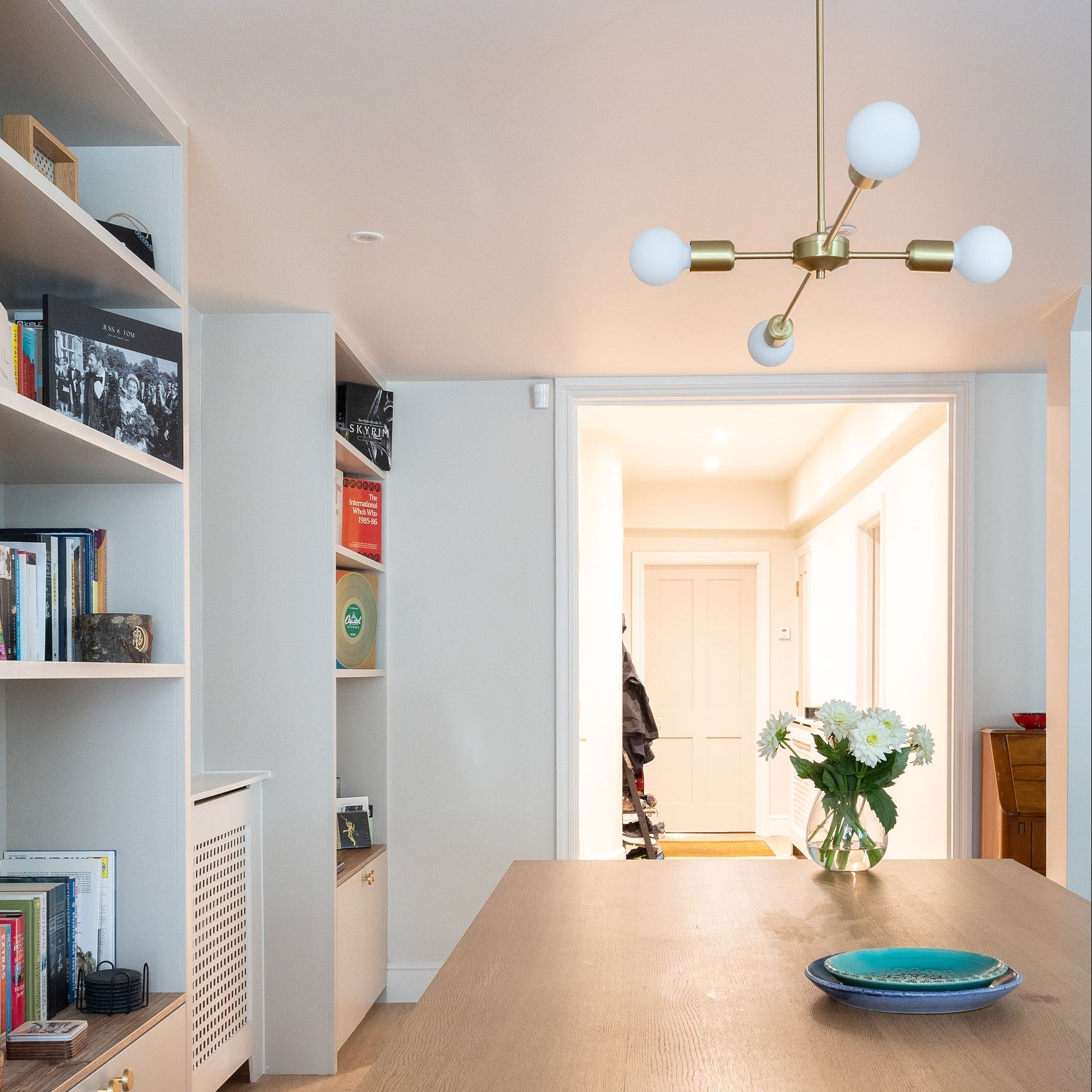 Modern interior with a dining table brass chandelier and bookshelves.