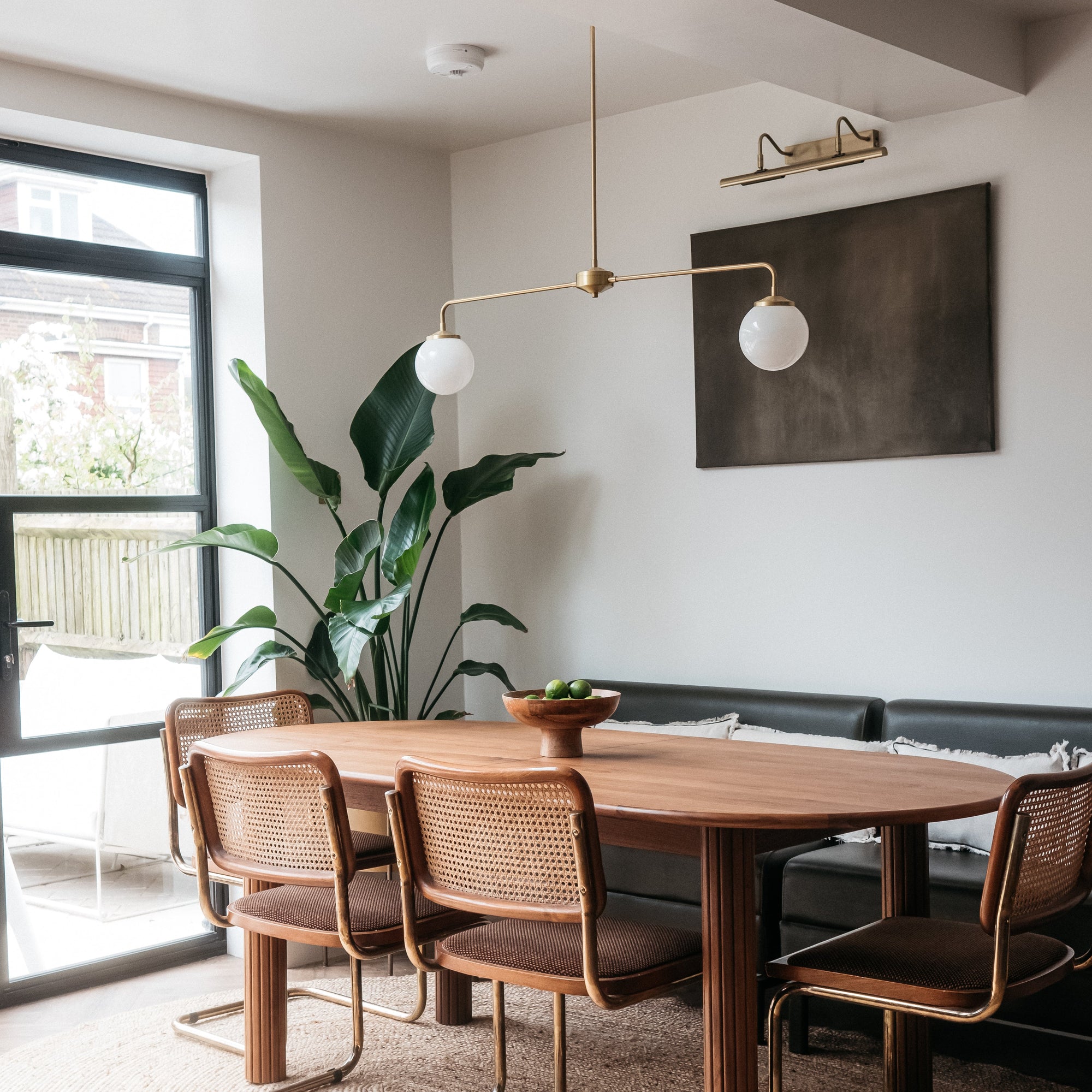 Dining area with wooden table and chairs in a modern interior setting and brass T-bar light